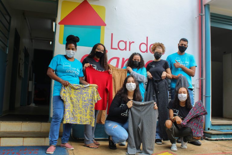 Jovens do Lar segurando as roupas sociais que receberam em campanha solidária do BTG Pactual.